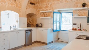 A modern kitchen with white cabinets, a dishwasher, and a blue-framed window. - Villa Oliva Sleeps 8 With Gym (Xaghra)
