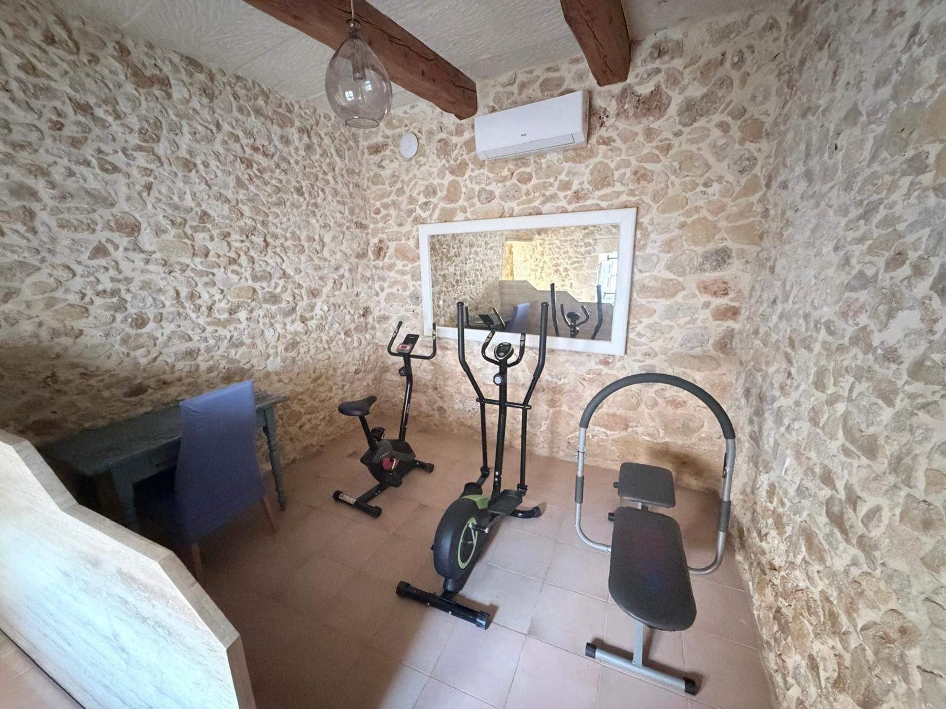 Habitació de parets de pedra amb ventilador de sostre, cinta de córrer, el·líptica i bicicleta estaciónia.