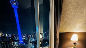 A hotel room with a large window offering a nighttime city view, including a prominent tower. - Vortex Suites KLCC by Rit Villa (Kuala Lumpur)