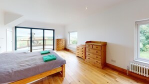 Un dormitorio con una cama grande, un aparador de madera y vistas al exterior a través de un ventanal corredero.