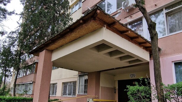 Un edificio de varios pisos con un porche cubierto y un pequeño jardín.