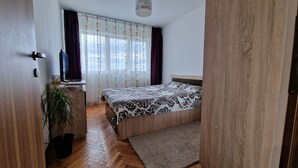 Un dormitorio con una cama de madera, un escritorio con silla, una planta en maceta y una ventana con cortinas.