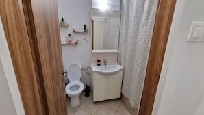Un baño pequeño con inodoro, lavabo y espejo. Hay estantes sobre el lavabo con artículos de aseo.