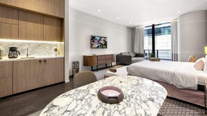 Une chambre d’hôtel moderne avec une table à manger en marbre, un canapé, un lit, une télévision et un coin cuisine.