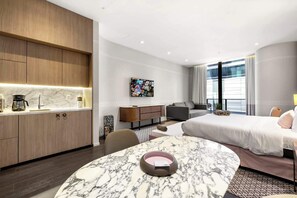 Een moderne hotelkamer met een marmeren eettafel, een bank, een bed, een televisie en een kitchenette.
