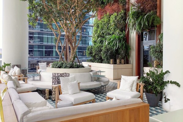A modern lounge area with white sofas, a central coffee table, and a variety of plants.