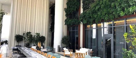 Vestíbulo de hotel con una larga recepción, área de estar con sillas y mesas, y un gran muro vertical de jardín interior.