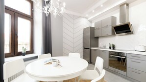 A modern kitchen with a round dining table, white chairs, a built-in oven, and a flat-screen TV above the counter. - Native Apartments Blich 7 (Kraków)