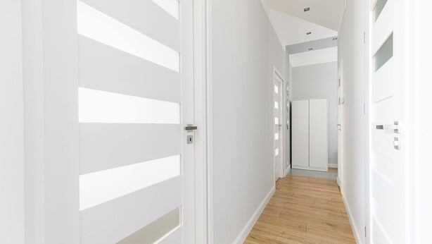 A modern hallway with white walls and wooden flooring, leading to a door with a handle. - Native Apartments Blich 7 (Kraków)