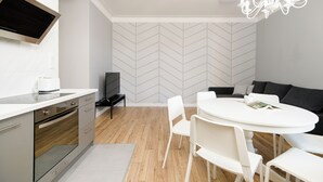 A modern kitchen with a built-in oven, a dining area with a round table and white chairs, and a grey sofa. - Native Apartments Blich 7 (Kraków)