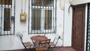 A small outdoor seating area with a table and chairs, a window with metal bars, and an air conditioning unit on the wall. - Freestyle Hostel Baku (Baku)
