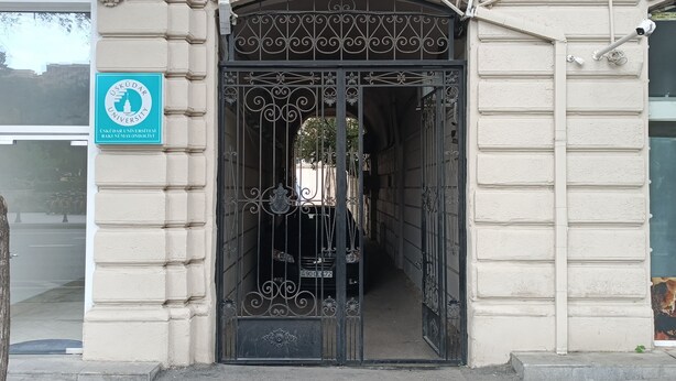 A building entrance with a decorative iron gate, a sign indicating it is a university, and a clear pathway leading to the entrance. - Freestyle Hostel Baku (Baku)