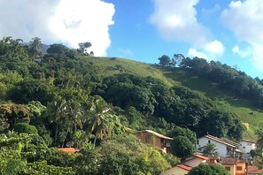 A hillside with lush greenery, a few buildings, and a clear sky. - Seasonal Beach House View to the Sea in Brazil (São Sebastião)