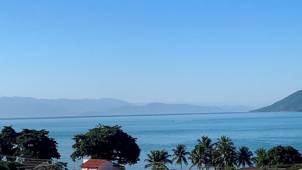 A coastal view with a clear sky, calm sea, and distant mountains. - Seasonal Beach House View to the Sea in Brazil (São Sebastião)