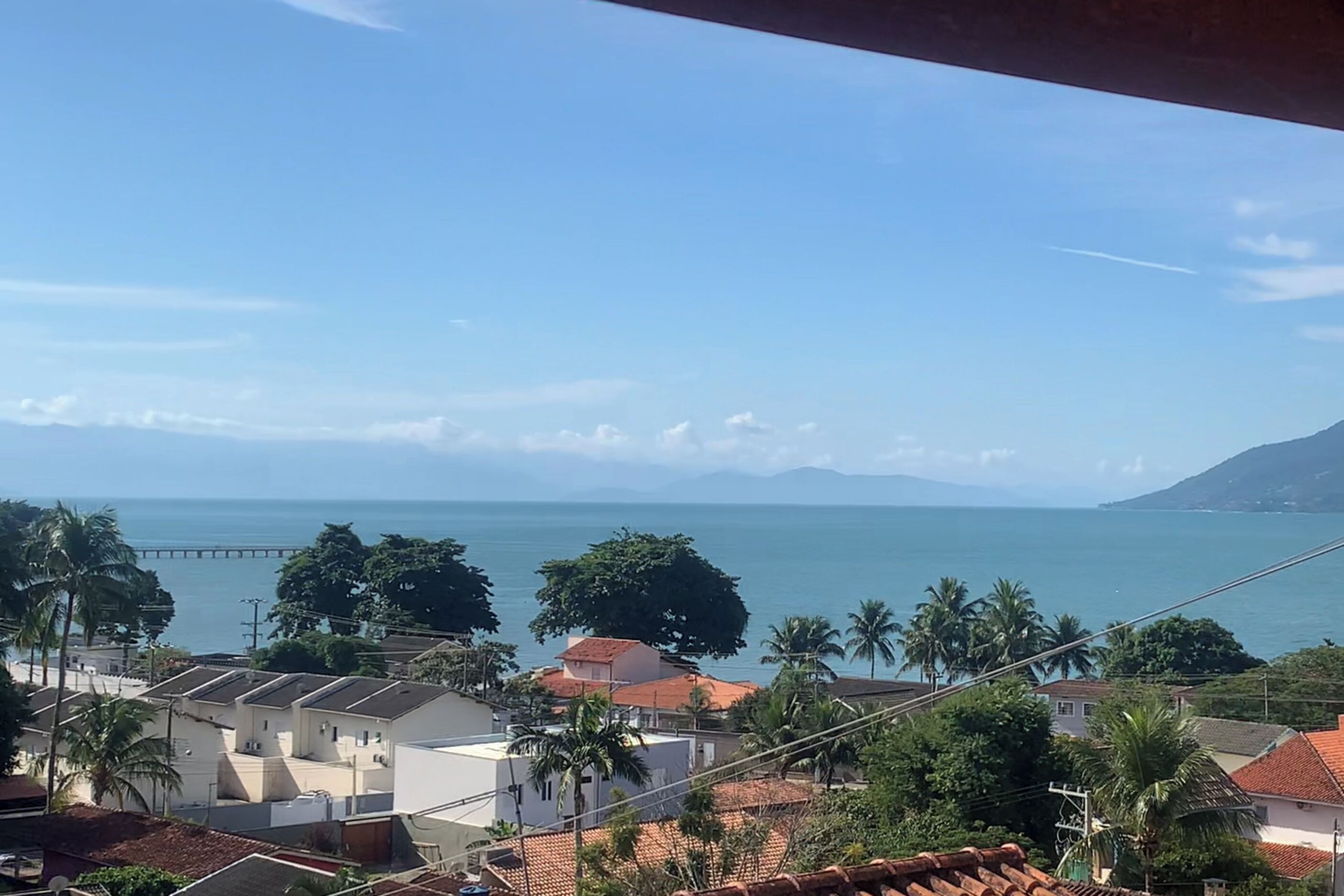 A coastal residential area with houses, palm trees, and a distant view of the sea and a bridge.