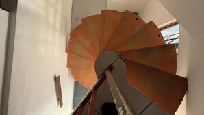 En spiraltrappe med gelænder i metal og en hvid væg.