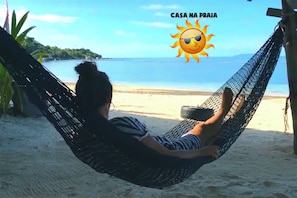 A hammock on a beach with a clear view of the sea and a tropical landscape in the background.