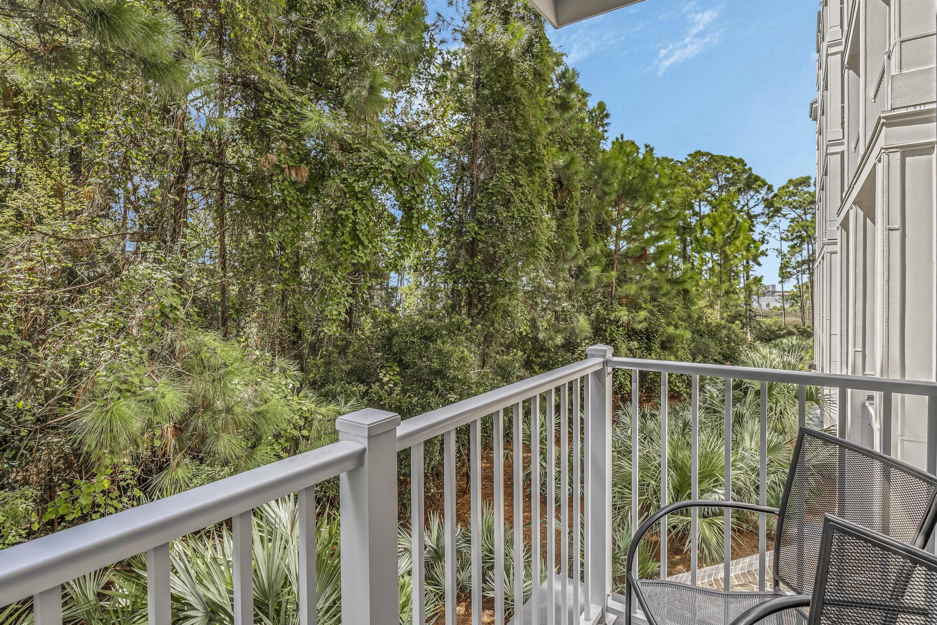A balcony with a white railing, overlooking a lush garden with various trees and plants.