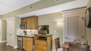 A compact kitchen with wooden cabinets, a microwave, a coffee maker, and a dining area with a chair and table. - Grand Comfort: 2 BR w/ Golf Cart & Bay Views at Sandestin Golf and Beach Resort! (Miramar Beach)