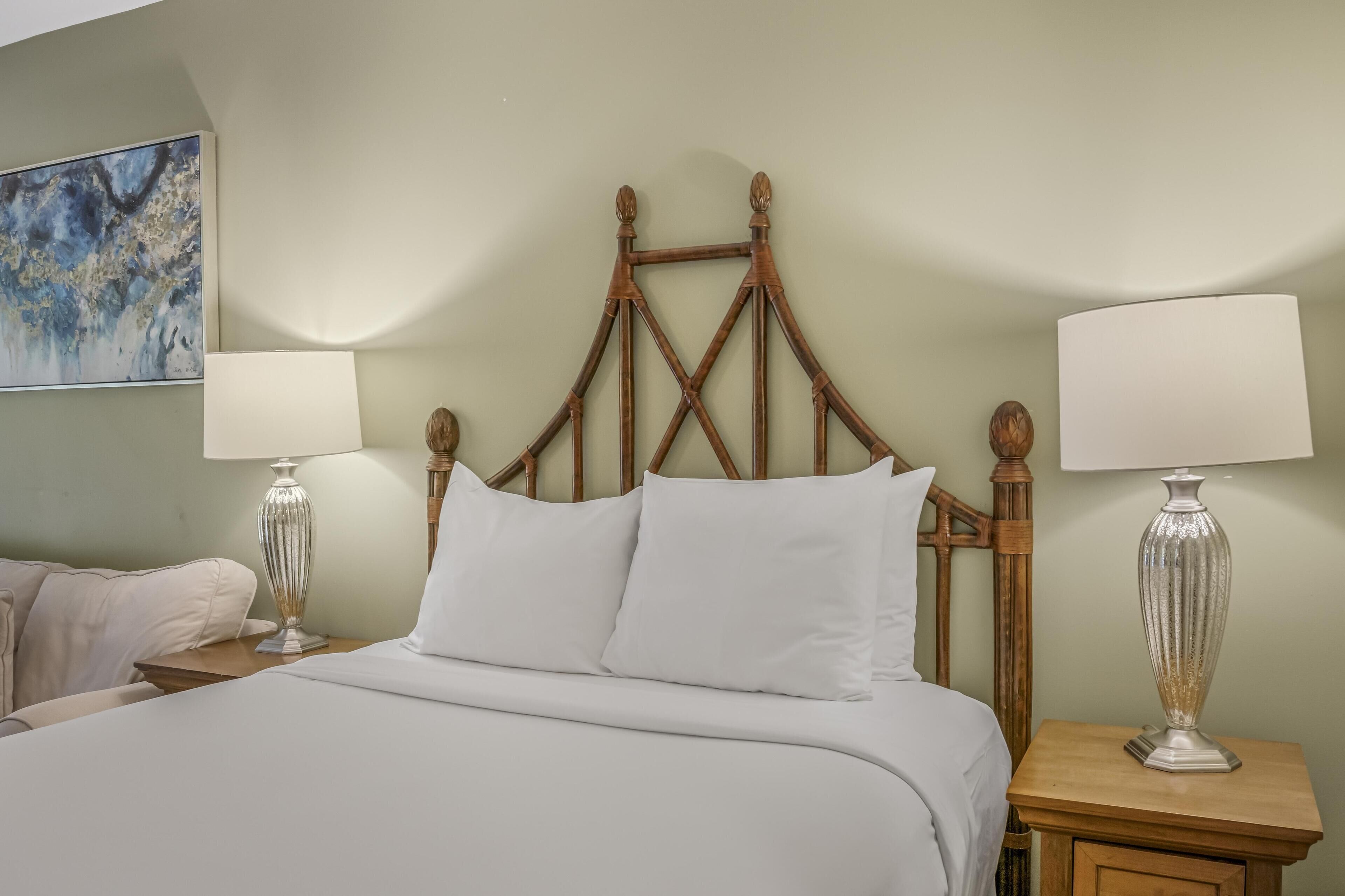 A neatly made bed with white linens, a wooden headboard, and two bedside lamps on wooden nightstands.