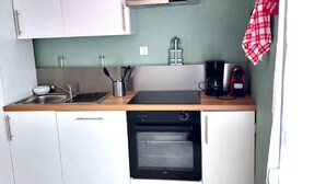 Une cuisine compacte avec des meubles blancs, un plan de travail en bois, un évier, une machine à café et une bouilloire.