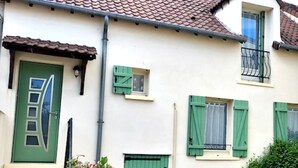 Une maison à deux étages avec une porte verte, des volets verts et un petit balcon.