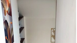 Un escalier menant à un palier avec une fenêtre, une petite table avec des tasses et un tableau encadré au mur.
