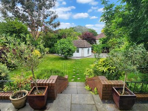 A garden with a white house, brick planters, and a clear sky. - London Family Home-amazing Garden (London)