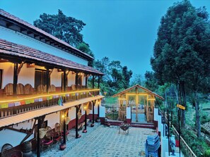 A traditional building with a tiled roof, a covered veranda with wicker furniture, and a small wooden structure in the background.