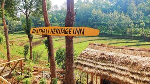 Un paesaggio rurale con un cartello che riporta "Balthali Heritage Inn" circondato da vegetazione rigogliosa e campi a terrazza.