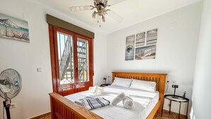 Een slaapkamer met een houten bed, een ventilator en uitzicht op een gebouw door een raam.