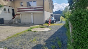 Una zona pavimentada con sistema de drenaje, un edificio con garaje y una bicicleta estacionada cerca.