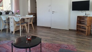 Una sala de estar moderna con comedor, un televisor montado en la pared y una estantería de madera.