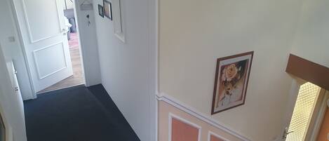 En hall med en trappa som leder upp till en våning ovanför. Väggarna är enkla och pryds av några få inramade tavlor.