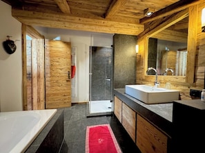 A modern bathroom with a wooden ceiling, a glass shower enclosure, a white bathtub, and a large mirror. - Kitzcharme Penthouse Ski & Golf by Belle-stay (Kitzbühel)