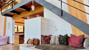 Uma sala de estar moderna com escada de madeira, um sofá com diversos almofadas e uma lareira.