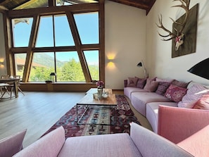 A spacious living room with a large window, a sofa set, a coffee table, and a wall-mounted deer skull. - Kitzcharme Penthouse Ski & Golf by Belle-stay (Kitzbühel)
