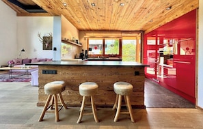 A modern kitchen with a wooden ceiling, a red accent wall, and a large window. - Kitzcharme Penthouse Ski & Golf by Belle-stay (Kitzbühel)
