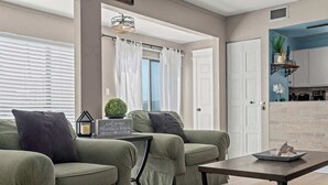 A living room with two green sofas, a coffee table, and a kitchen visible through an open door. - Catching Rays-Heated Pool-Family and Pet Friendly (Destin)
