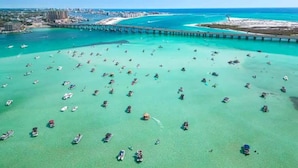 An aerial view of a coastal area with numerous boats, a pier extending into the water, and a distant cityscape. - Catching Rays-Heated Pool-Family and Pet Friendly (Destin)