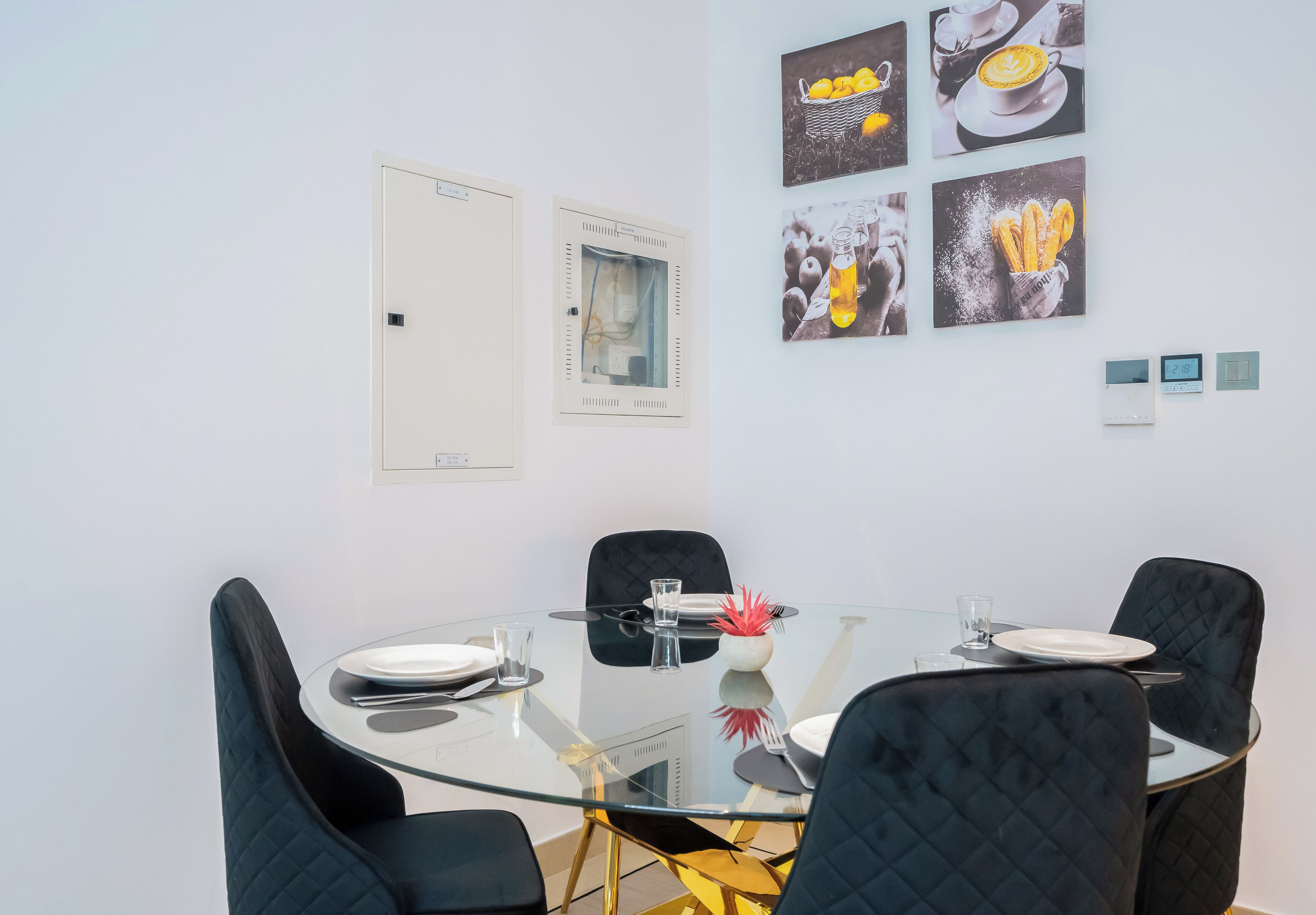 A modern dining area with a glass table, black cushioned chairs, and a whiteboard on the wall.