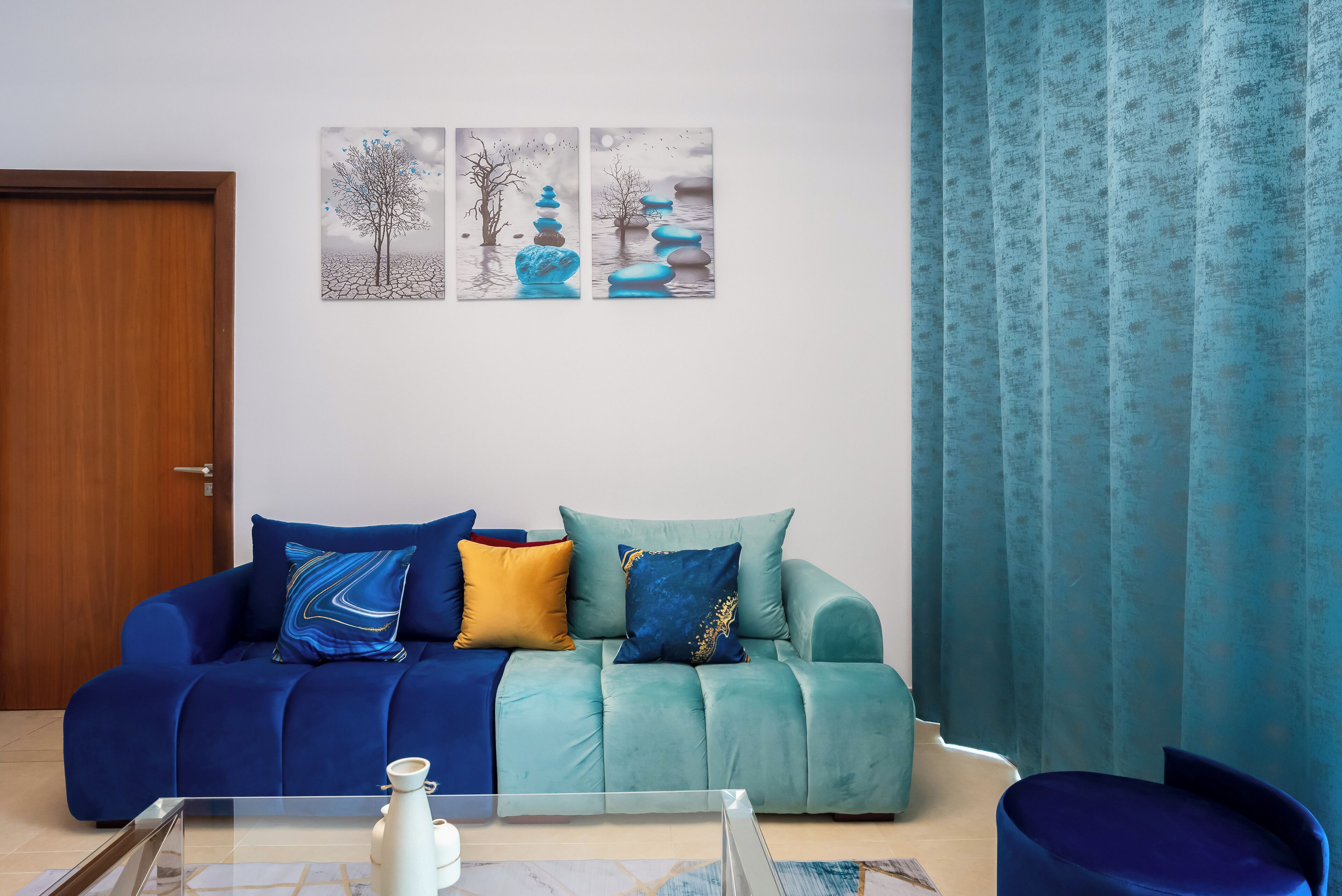 Ein Wohnzimmer mit einer Couch, einem Couchtisch und einem blauen Sessel. An den Wänden hängen zwei Gemälde.