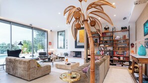 A modern living room with a large bookshelf, a fireplace, and a large window overlooking a garden. - Futuriste - Exceptional residence with panoramic view (Saint-Didier-au-Mont-d'Or)
