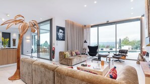 A modern living room with a large sofa, a black chair, and a coffee table. There is a large window with a view of the outdoors. - Futuriste - Exceptional residence with panoramic view (Saint-Didier-au-Mont-d'Or)