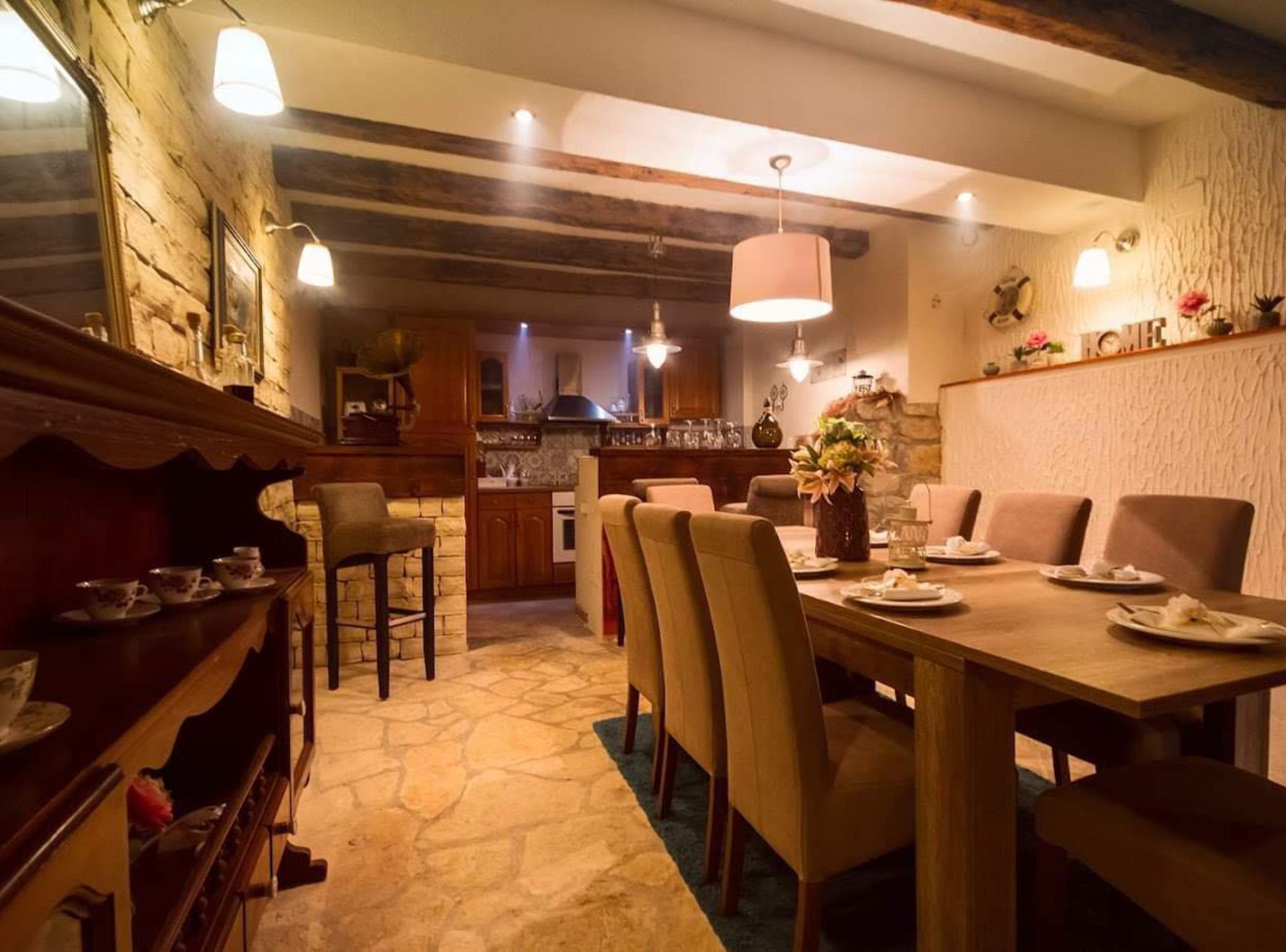 A cozy dining area with a stone floor, wooden furniture, and a kitchen in the background.