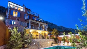 Ένα διώροφο κτίριο με πισίνα, πέτρινα τοίχους και εξωτερικό χώρο για καθιστικό.