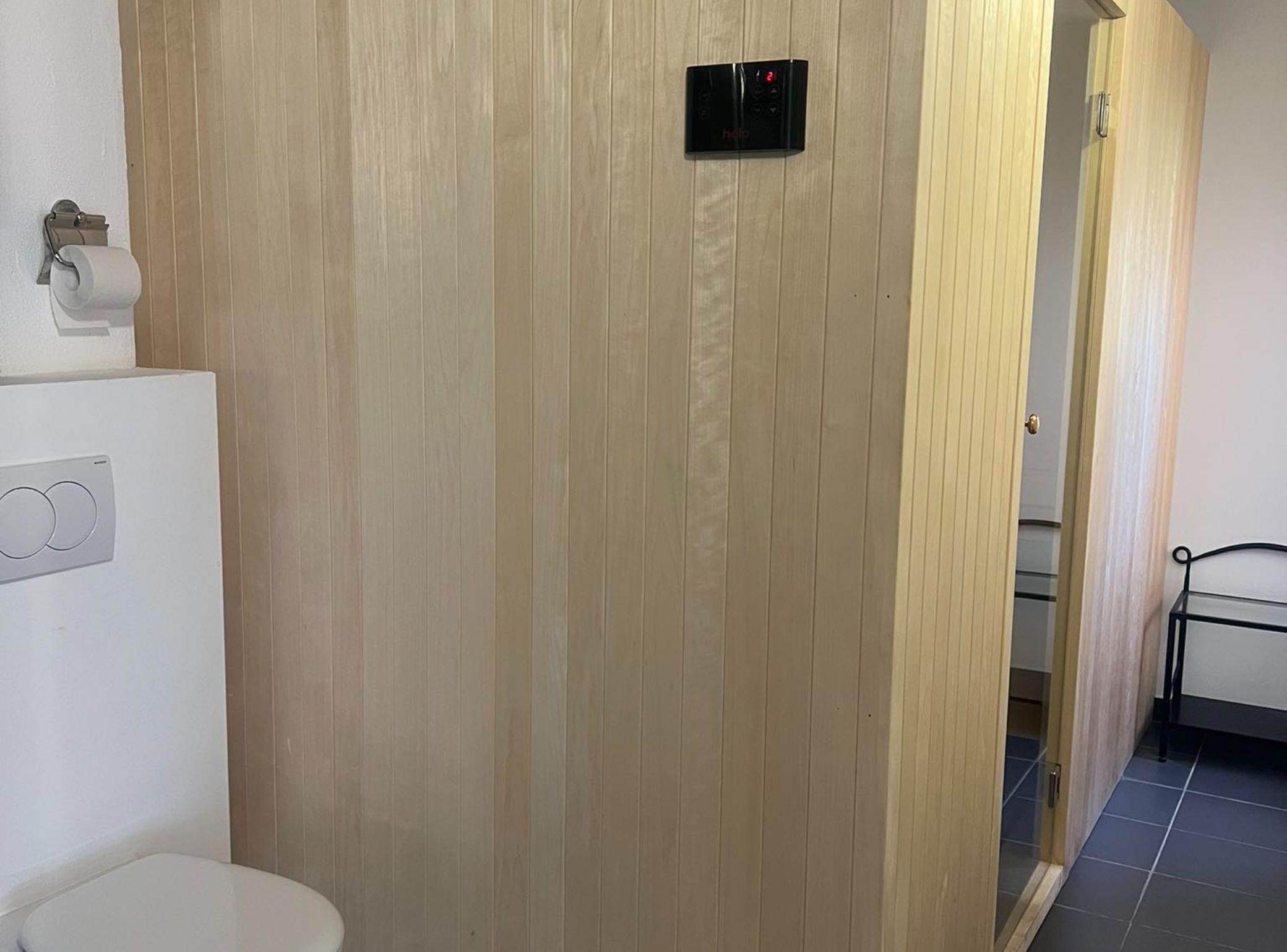 Een badkamer met een wand van houtpanelen, een toilet, een handdroger en een bedieningspaneel.