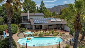 Une maison avec une piscine, des panneaux solaires et un paysage montagneux en toile de fond.