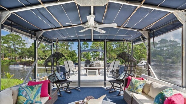 A covered outdoor seating area with a ceiling fan, wicker furniture, and a view of a body of water. - Pura Vida- Floating Home (Merritt Island)