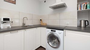 A compact kitchen with a washing machine, a coffee maker, and a kettle on the countertop.